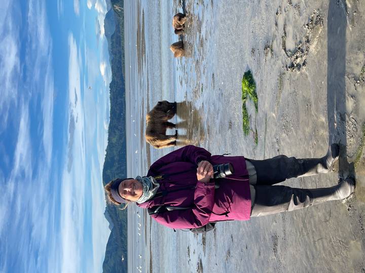 Persona de pie en marismas con un oso en el fondo.