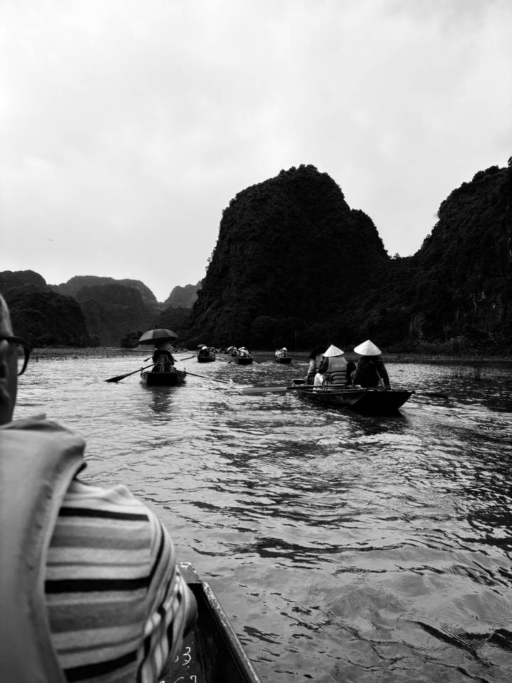 Row of boats in a scenic river with people rowing traditional hats.