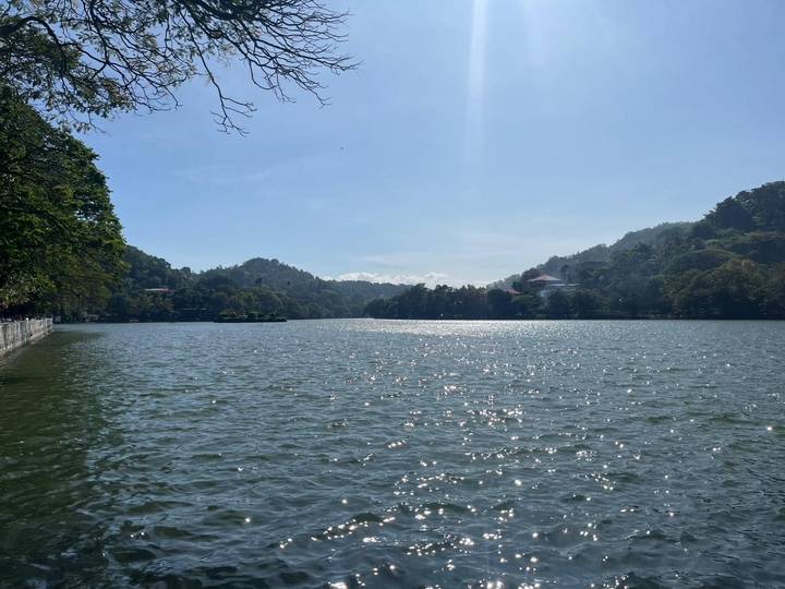 A scenic view of a lake surrounded by hills and trees under a clear blue sky.