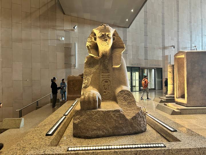 Une statue d'un Sphinx dans un musée avec des gens qui l'observent.