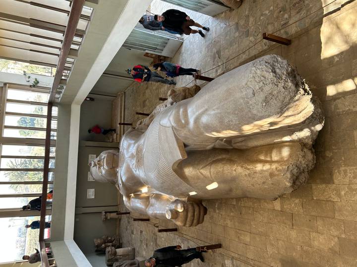 Grande statue d'une figure allongée dans un musée avec des gens autour