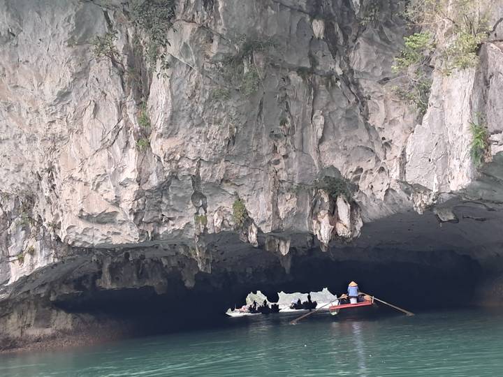 Bote de remos acercándose a la entrada de una cueva en un acantilado de piedra caliza
