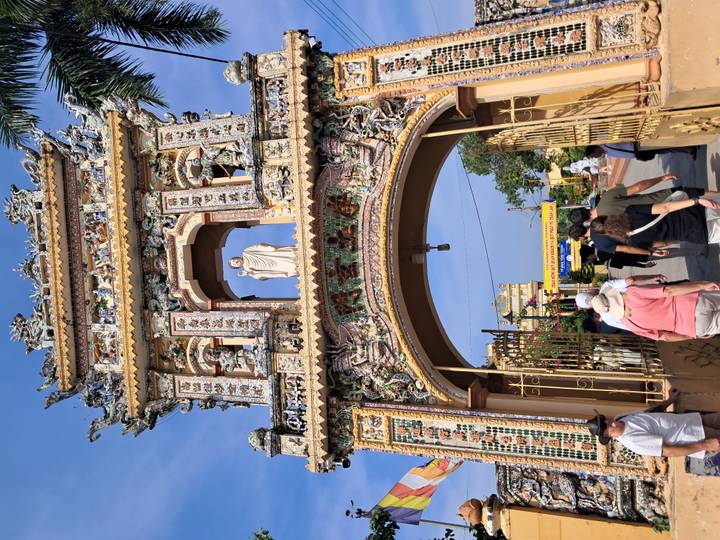 Puerta de templo intrincadamente decorada con una estatua, gente reunida abajo.