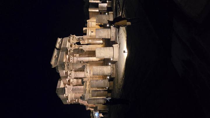 Ancient temple ruins illuminated at night with columns and statues.