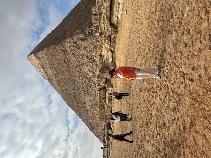 Person standing in front of a pyramid, with others in background.