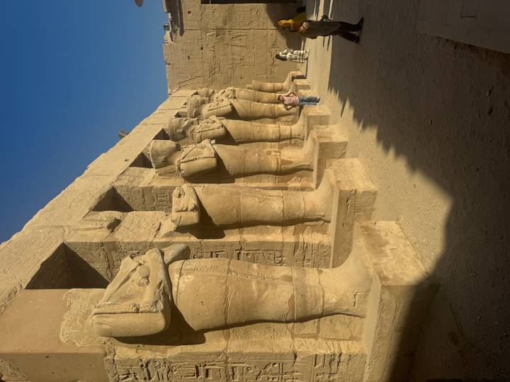 Row of statues against an ancient temple wall with few people.