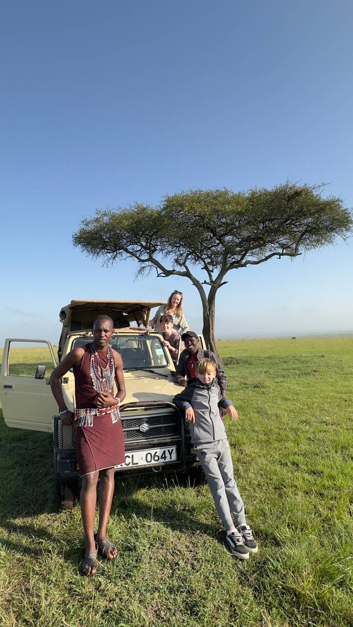Personas posando junto a un vehículo de safari bajo un árbol