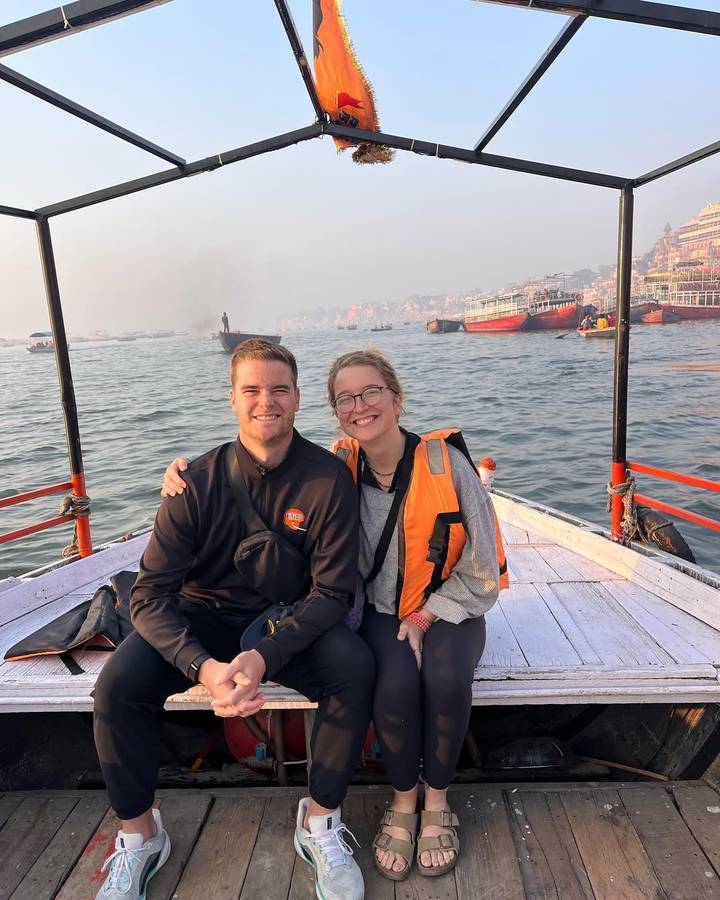 Pareja sentada en un barco con un puerto fluvial bullicioso en el fondo.