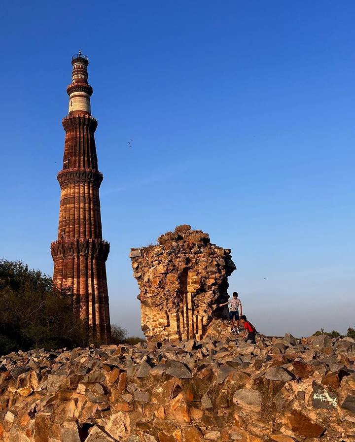 Persona de pie cerca de monumento antiguo y ruinas de ladrillo bajo un cielo azul claro.
