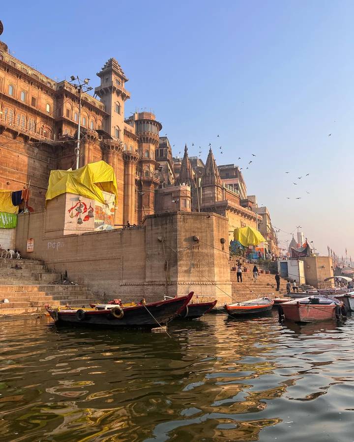 Antiguos ghats a lo largo de un río con barcos y edificios.