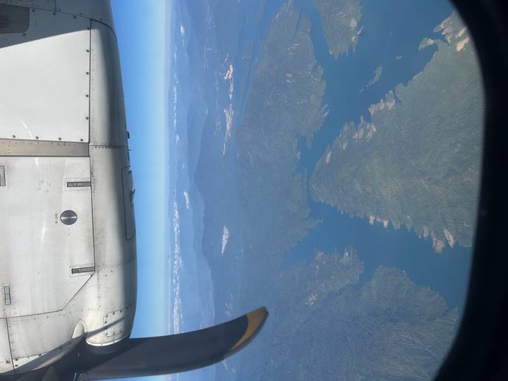 Vista aérea desde la ventana de un avión mostrando montañas y vías navegables.