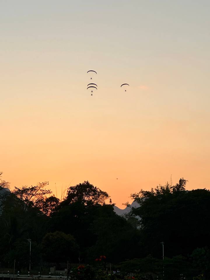 Parapentistas silueteados contra un cielo de atardecer sobre un paisaje sereno.