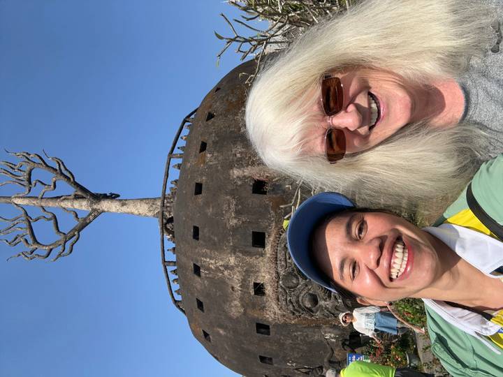Dos personas sonriendo frente a una escultura de árbol inusual.