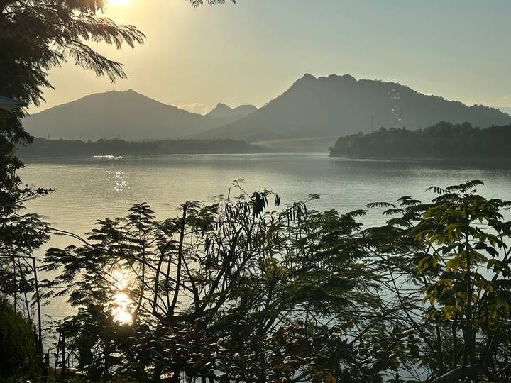 Lago sereno rodeado de montañas bajo un sol poniente.