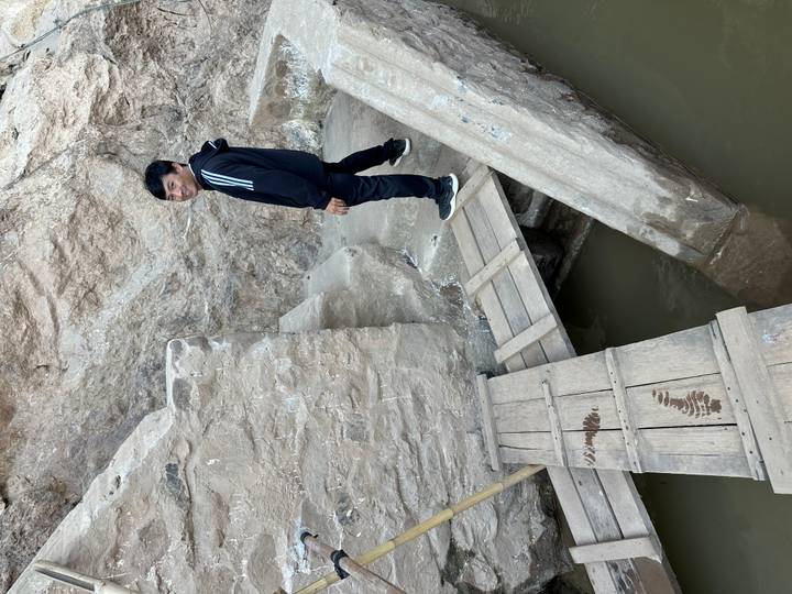 Persona navegando por un puente de madera improvisado sobre una pequeña masa de agua.