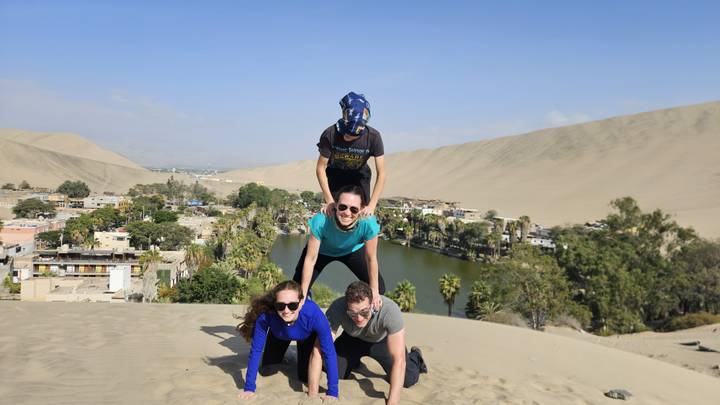 Cuatro personas formando una pirámide encima de una duna de arena.