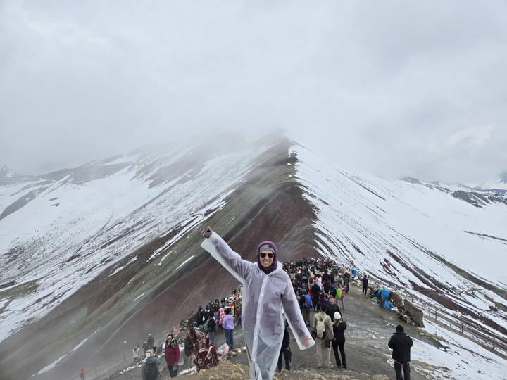 Persona posando frente a una montaña nevada con una multitud.