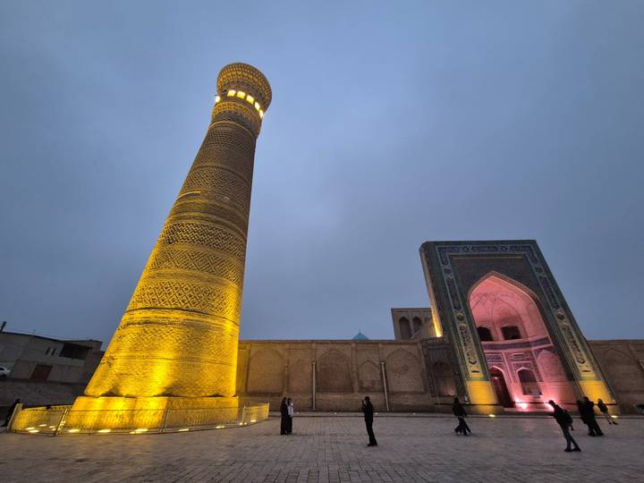 Illuminated minaret and mosque facade in Bukhara at dusk.