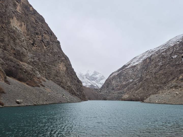 Serene lake surrounded by mountainous terrain and snow on peaks.
