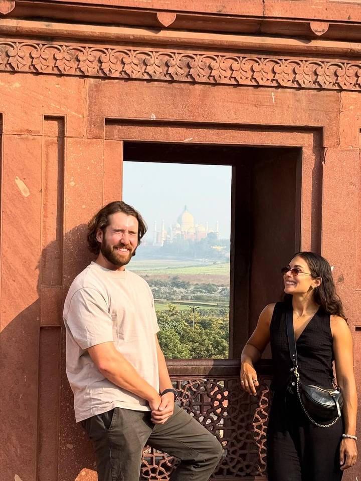 Dos personas paradas en un lugar pintoresco con el Taj Mahal visible al fondo.