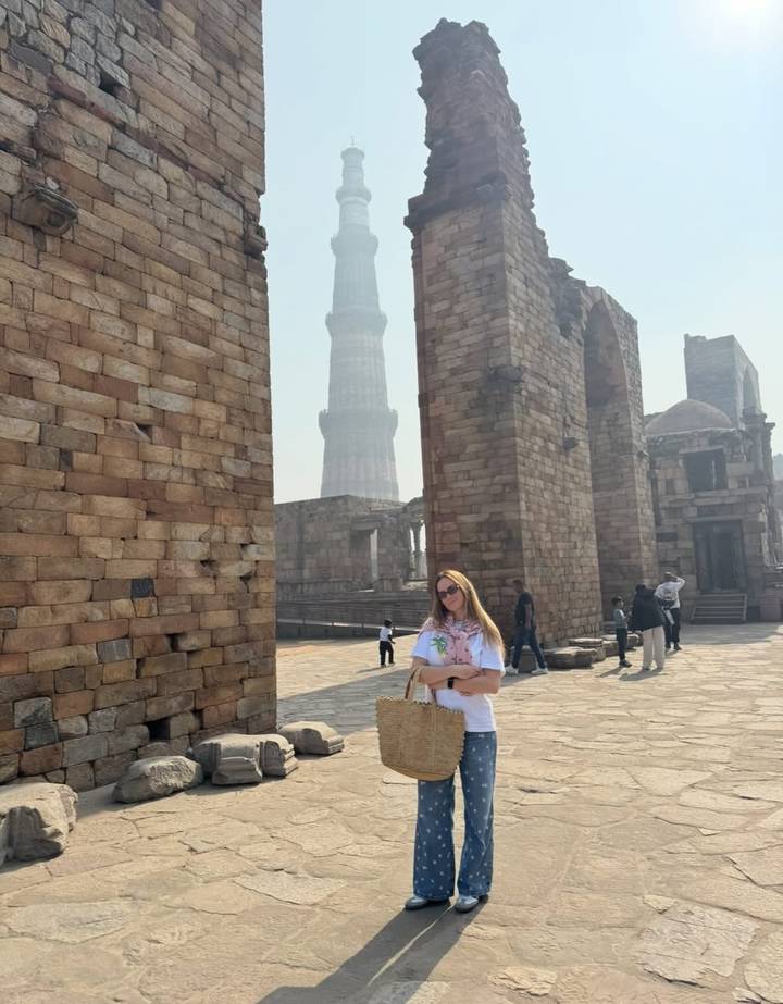 Femme posant devant un monument historique avec une haute structure en pierre.
