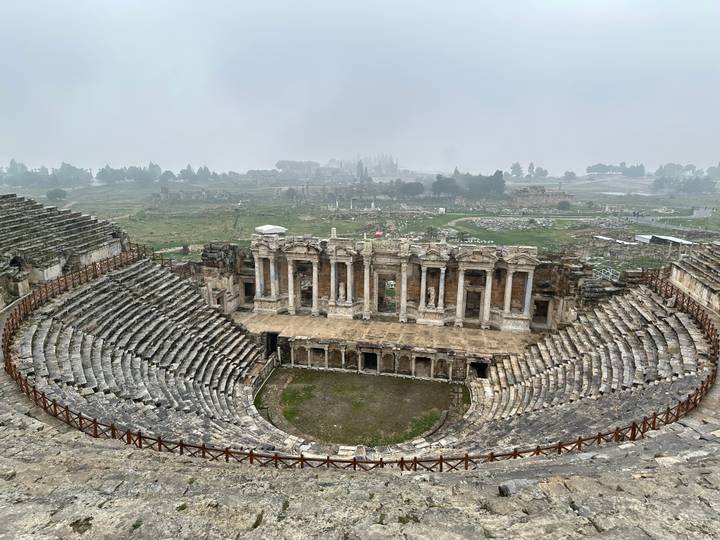 Ruines d'un amphithéâtre antique sous un ciel nuageux.