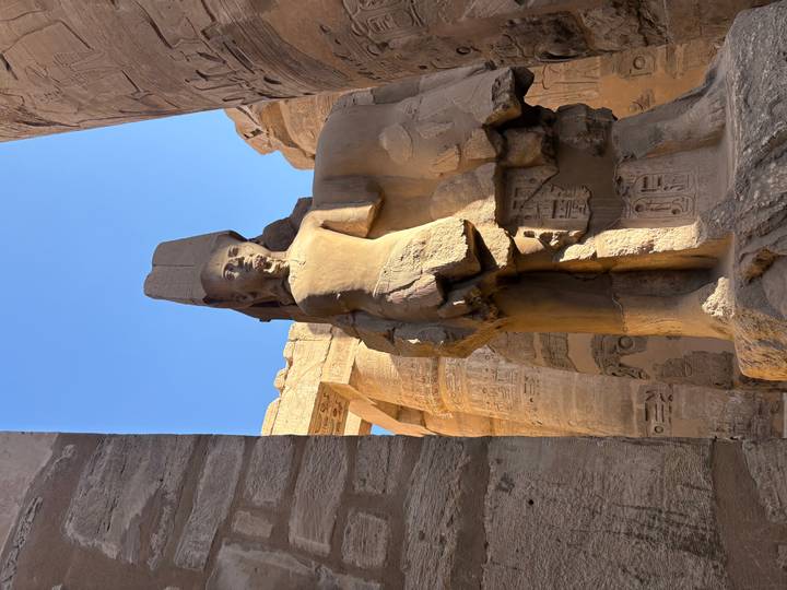 Ancient Egyptian statue and columns under a clear blue sky.