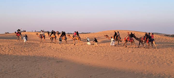 Des gens chevauchant des chameaux à travers les dunes de sable.