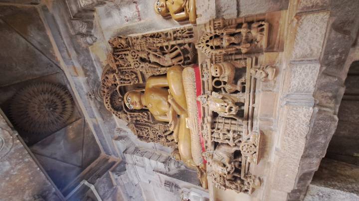 Statue d'une divinité assise dans une alcôve ornée de sculptures.