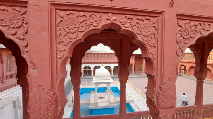 Vue à travers des arcs rouges ornés d'une cour intérieure avec une fontaine.