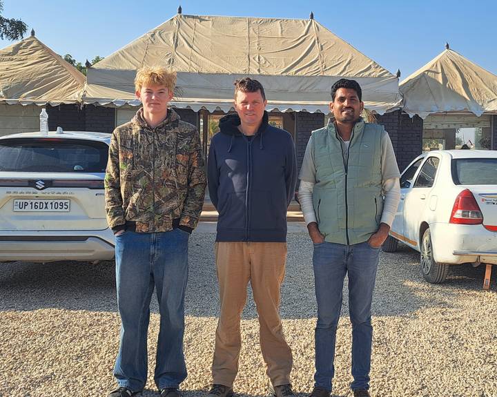 Trois hommes debout devant des tentes dans un camp du désert.