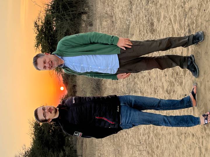 Dos personas posando en un paisaje desértico al atardecer.