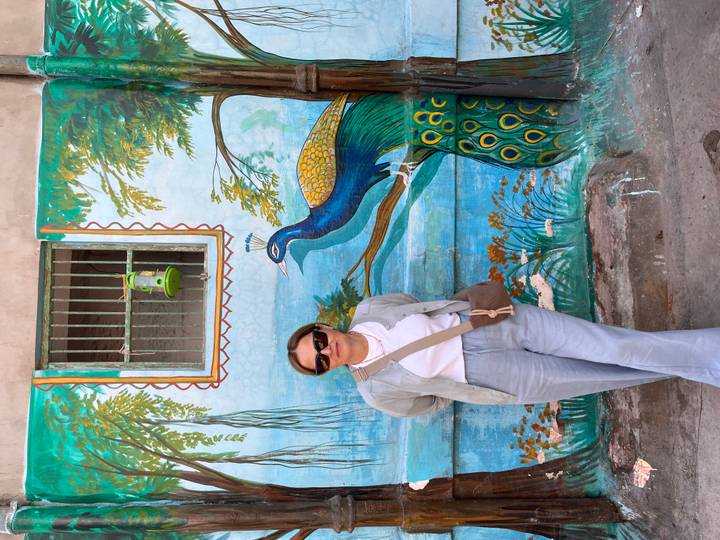 Mujer posando frente a un mural de pavo real en una pared.