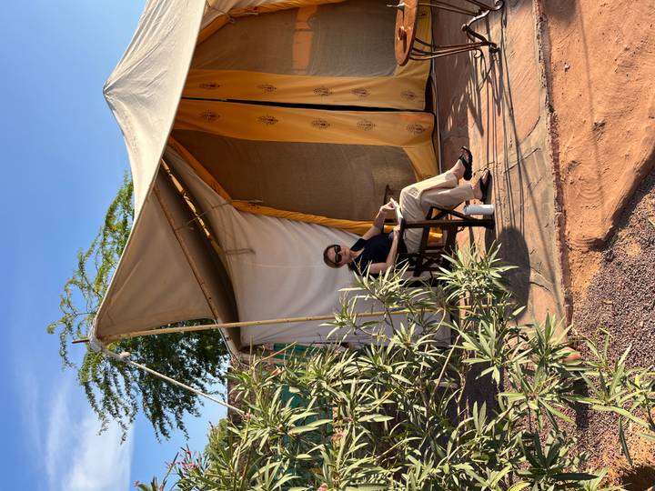 Mujer sentada frente a una tienda de campaña de lona en una zona desértica.