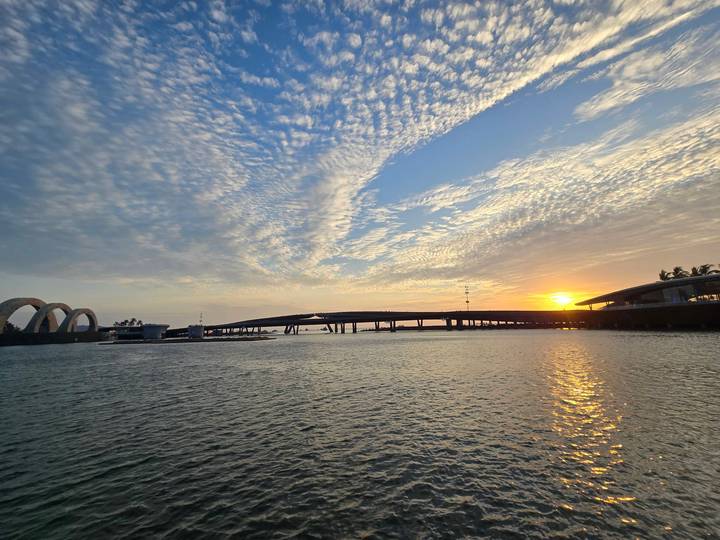 Atardecer sobre un río con un puente y nubes dramáticas.