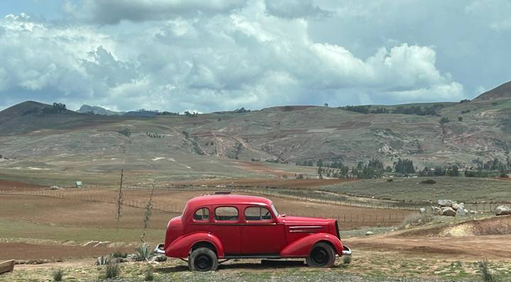Vintage red car parked in a rural landscape.