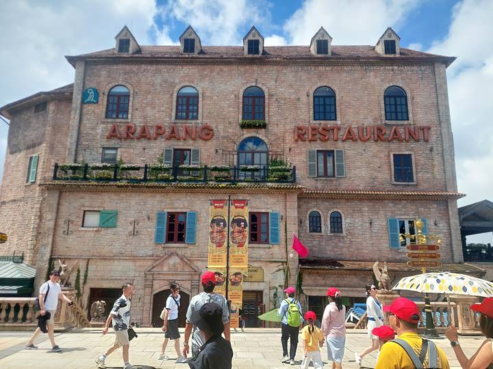 Personas caminando afuera de un edificio de restaurante de piedra con el letrero 'ARAPANG RESTAURANT'.