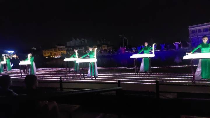 Escena nocturna borrosa de actuación con personas en atuendo tradicional.