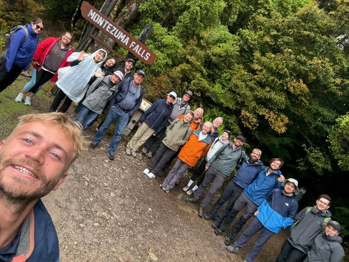Group of people posing at a natural site with trees in the background.