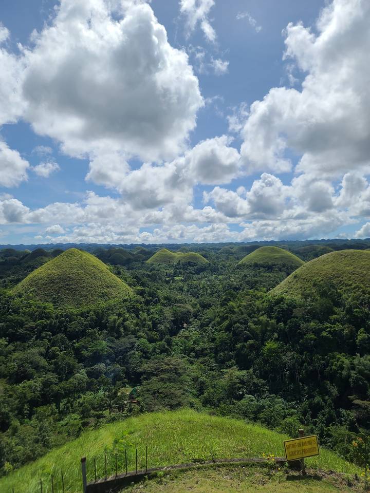 Une vue panoramique des Chocolate Hills sous un ciel nuageux.
