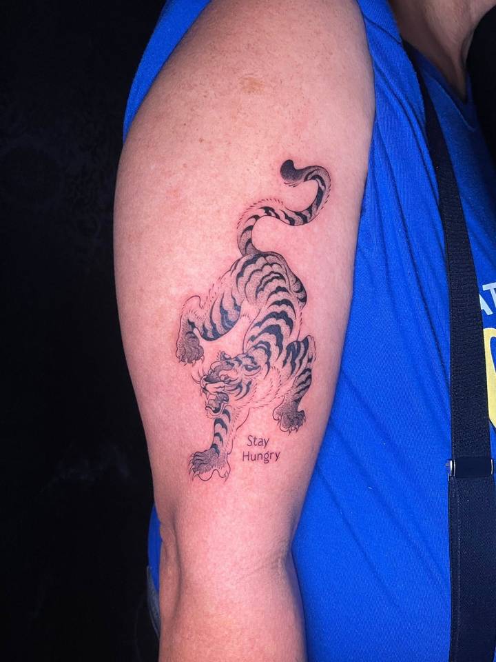 Un primer plano de un tatuaje en el brazo de una persona que muestra un tigre con las palabras 'Stay Hungry'.