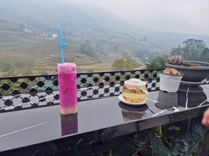 Una bebida y un postre sobre una mesa con vista a colinas en terrazas.