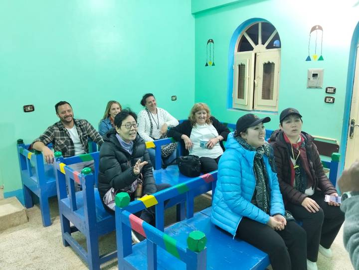Group of people sitting indoors on colorful benches.