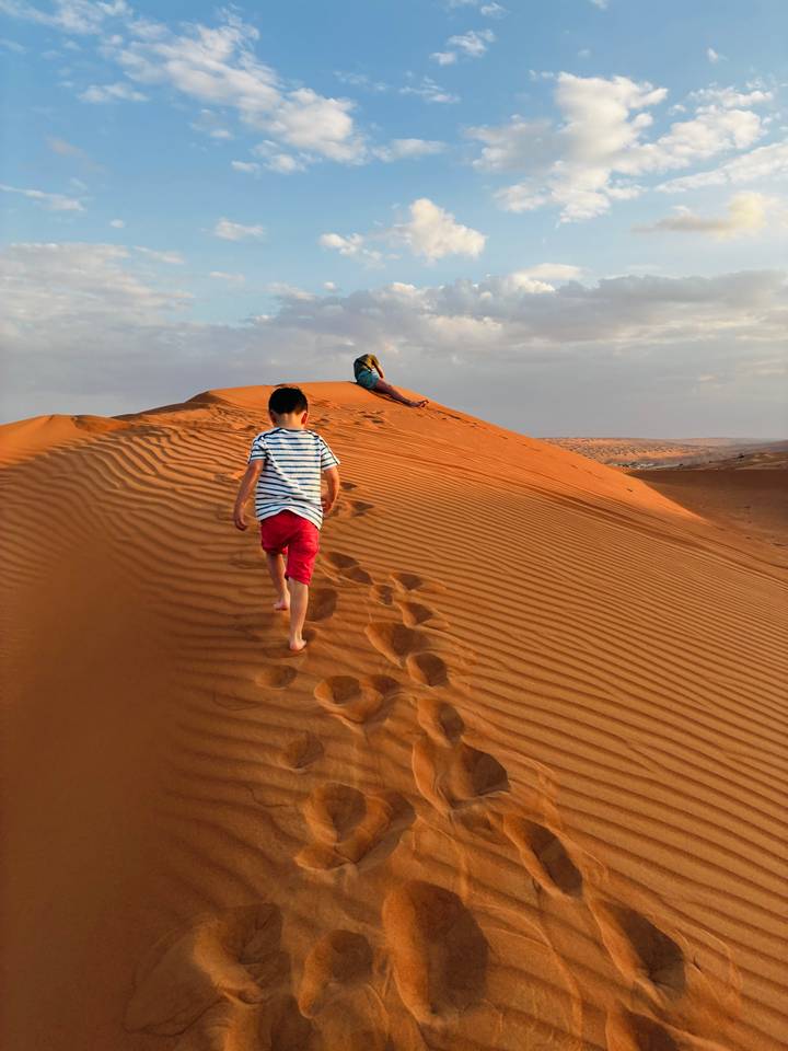 Des enfants grimpant sur les dunes de sable au coucher du soleil.