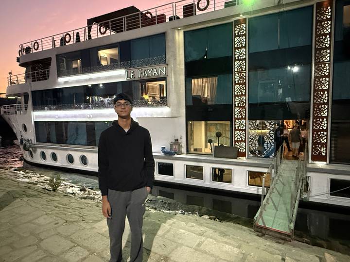 Person standing in front of an illuminated river cruise ship at dusk.