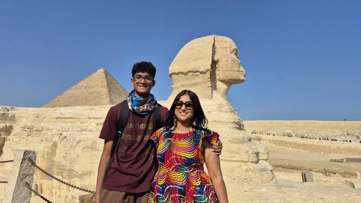 Visitors posing in front of the Sphinx and Pyramid, under a clear blue sky.