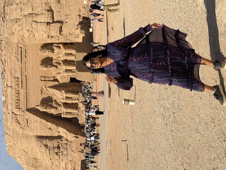Tourist posing in front of Abu Simbel temple, with large statues carved into the rock.