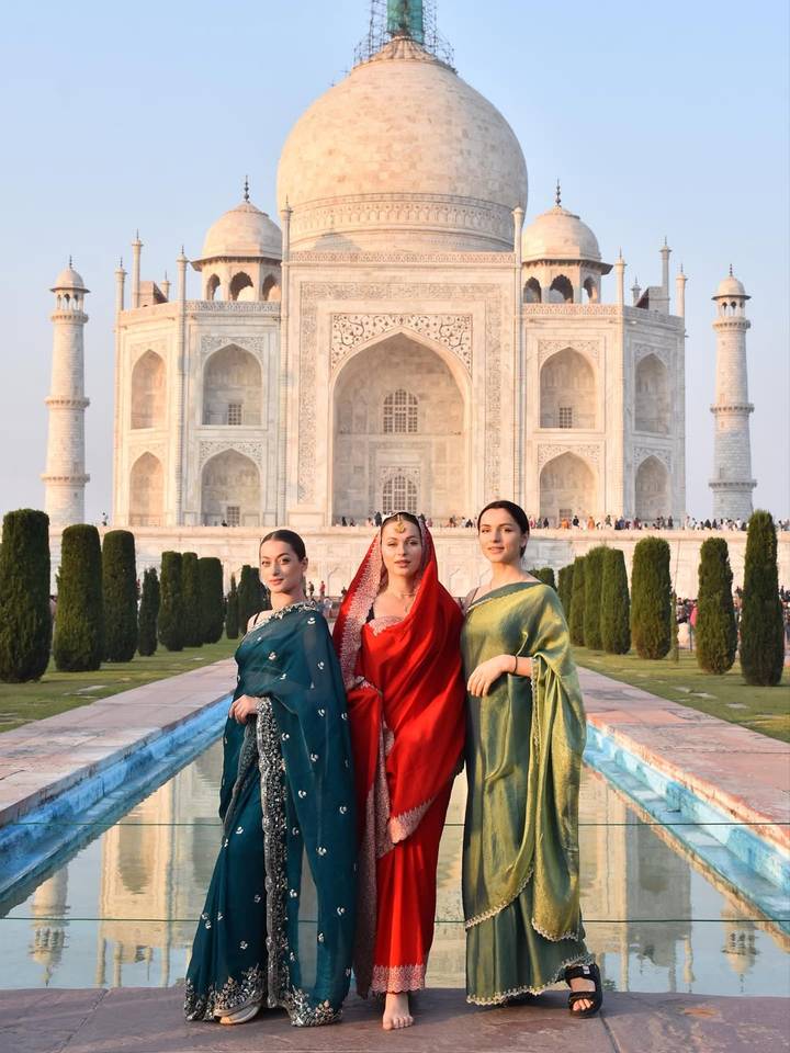 Trois personnes en tenue traditionnelle se tiennent debout devant le Taj Mahal.
