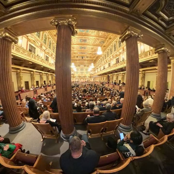 Personas asistiendo a un evento dentro de un gran salón con decoraciones elaboradas.