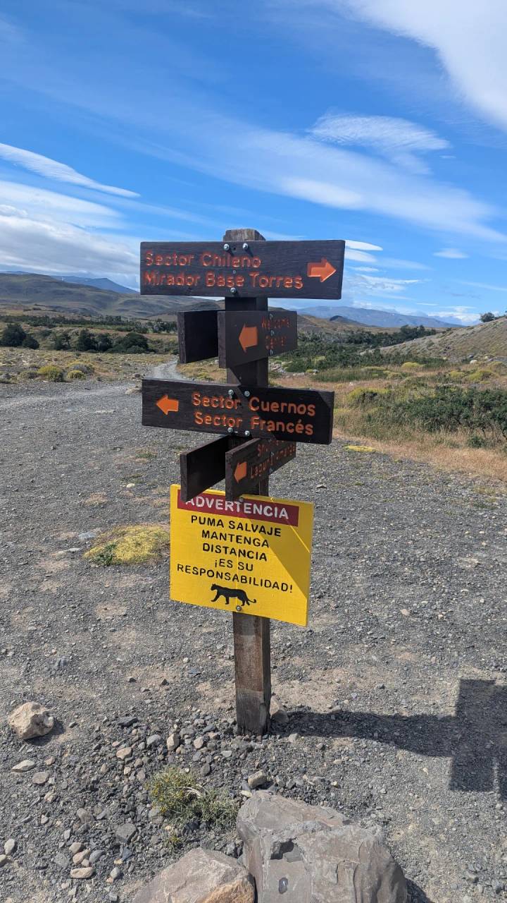 Poste direccional en un sendero con señal de advertencia debajo.